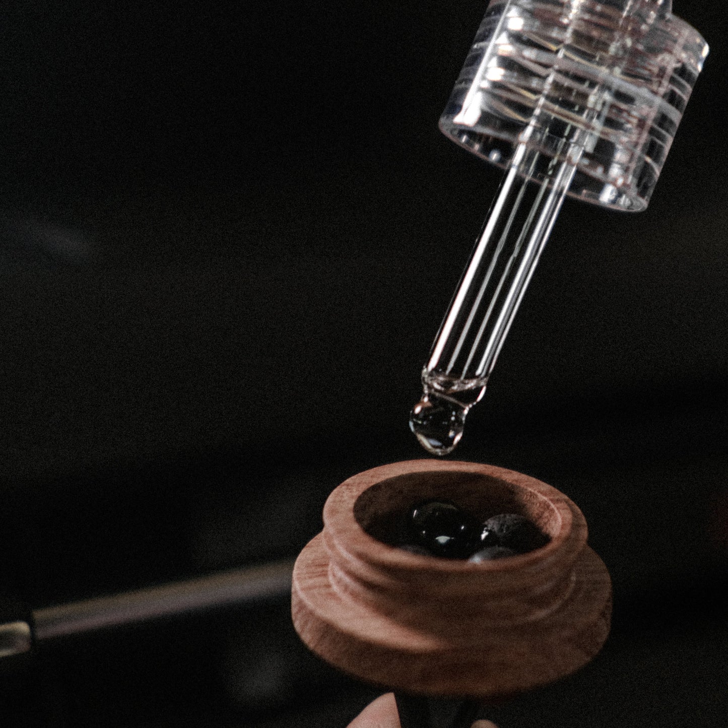 Glass dropper with liquid being applied to a wooden container against a dark background