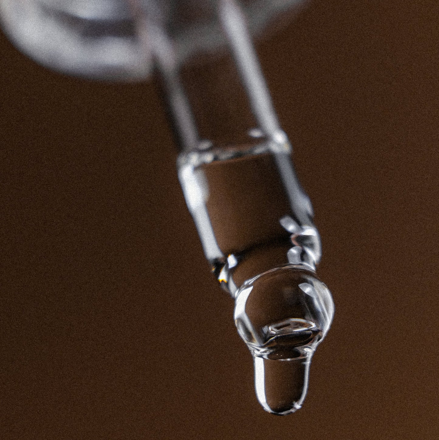 Close-up of a glass dropper with a brown background
